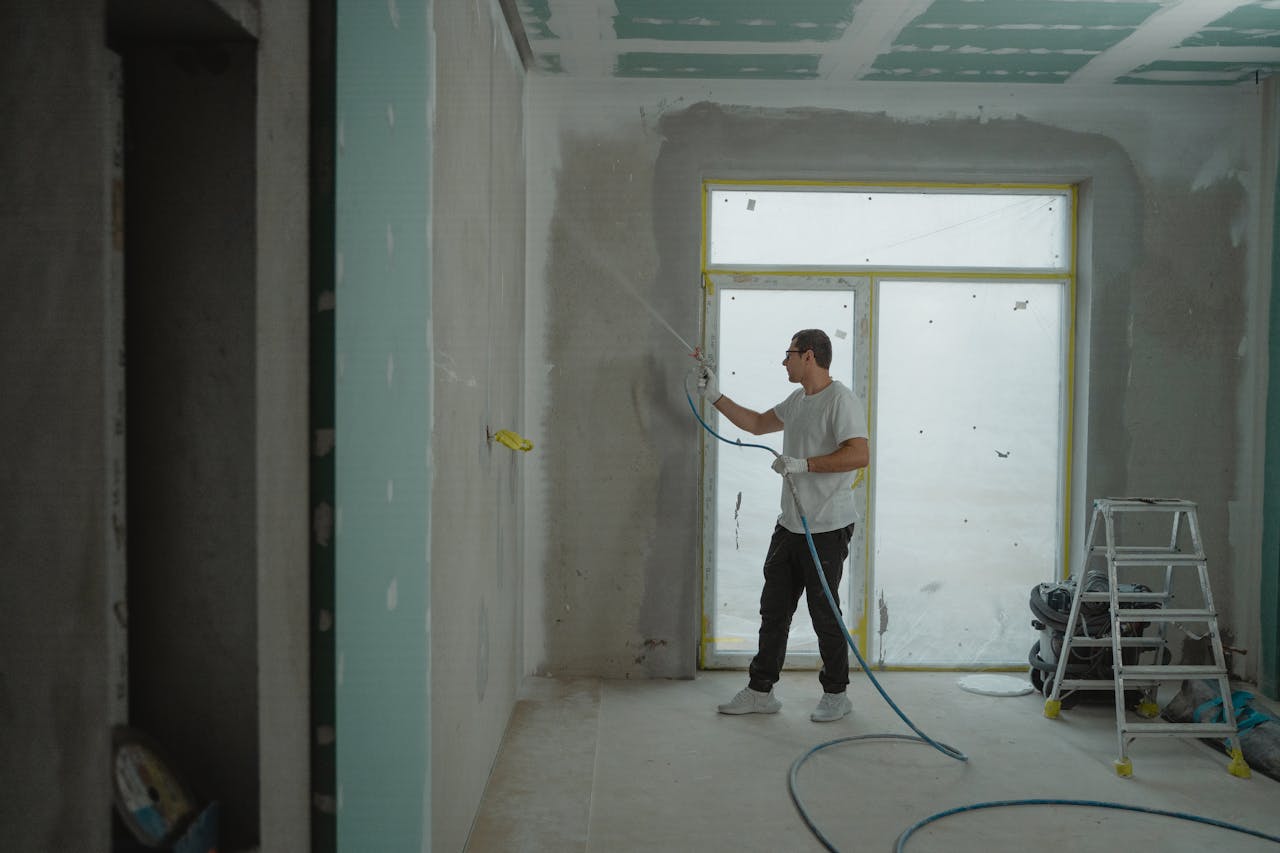 Services-02 A man sprays paint on a wall while renovating an indoor room with professional equipment.