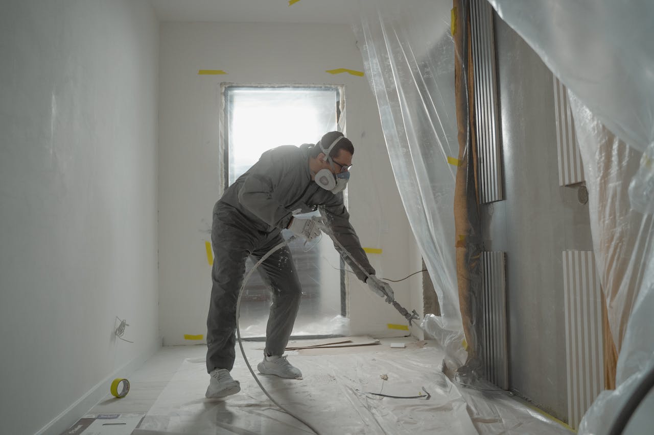 digital A worker in protective gear painting walls during an indoor renovation project.